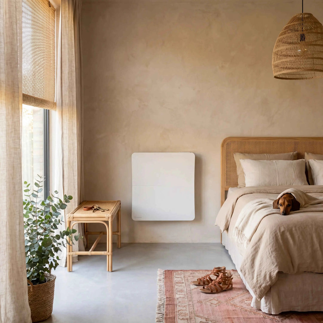 Radiatore Cira da 1000 W bianco fissato alla parete di una camera da letto, tra uno sgabello in rattan e il letto